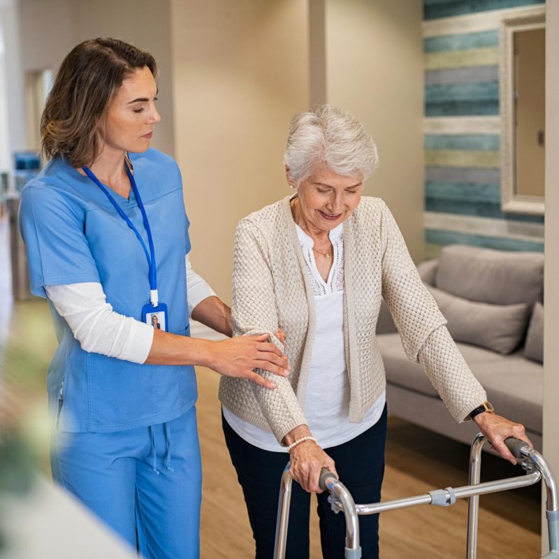 Lovely,Nurse,Helping,Old,Woman,To,Walk,At,Nursing,Home